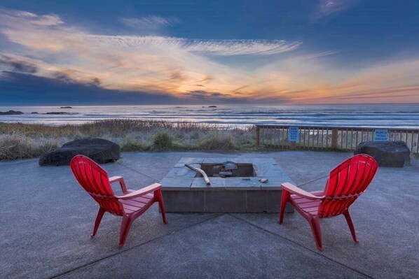 A concrete patio with two red Adirondack chairs facing a wooden deck overlooking the ocean.