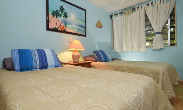 Una habitación con dos camas, una lámpara, un cuadro y una ventana con cortinas.