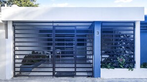 Un edificio moderno con un portón metálico grande, una pared azul y algo de vegetación.