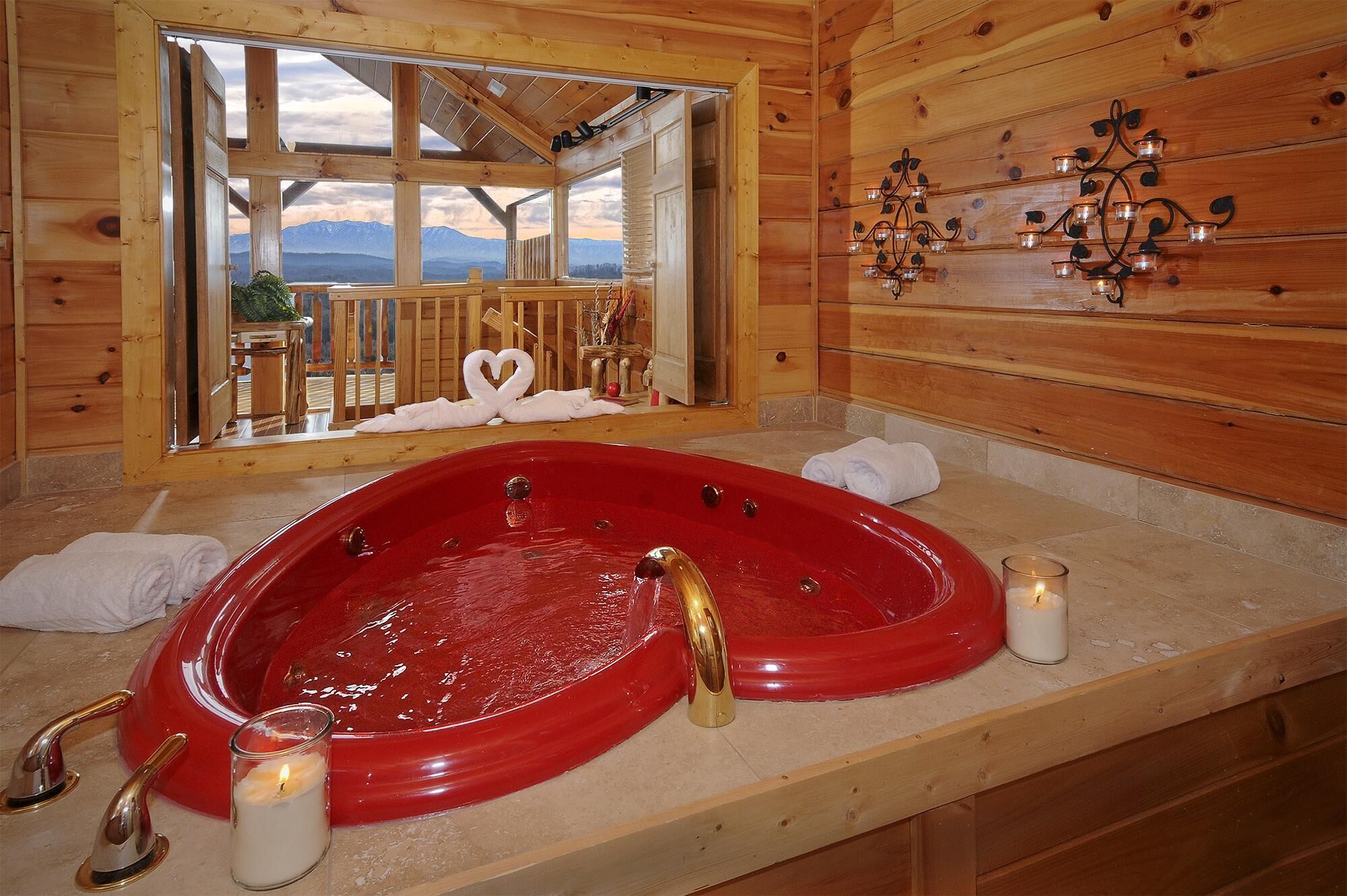 Ein Badezimmer einer Holzhütte mit einer roten Badewanne, einem großen Spiegel und Bergblick durch das Fenster.