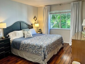 Un dormitorio con cama, mesitas de noche, cortinas en la ventana y vistas a zonas verdes.