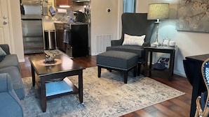 A living room with a sofa, a coffee table, a chair with a pillow, a lamp, and a rug. - Sophie’s Cottage with Private Garden - Walk to Old Town Roseville (Roseville)