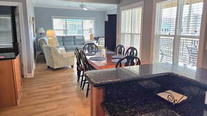 A spacious kitchen with a granite countertop, a dining area with a wooden table and chairs, and a living room with a sofa and a lamp. - Beautiful condo. Short walk to the beach!  Linens & Towels included. Beds Made! (Ocean Isle Beach)