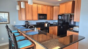 A modern kitchen with wooden cabinets, a black refrigerator, a microwave, and a built-in island with bar stools. - Beautiful condo. Short walk to the beach!  Linens & Towels included. Beds Made! (Ocean Isle Beach)