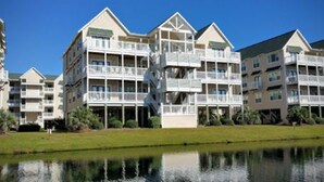 A multi-story hotel with balconies, a swimming pool, and a reflection in the water. - Beautiful condo. Short walk to the beach!  Linens & Towels included. Beds Made! (Ocean Isle Beach)