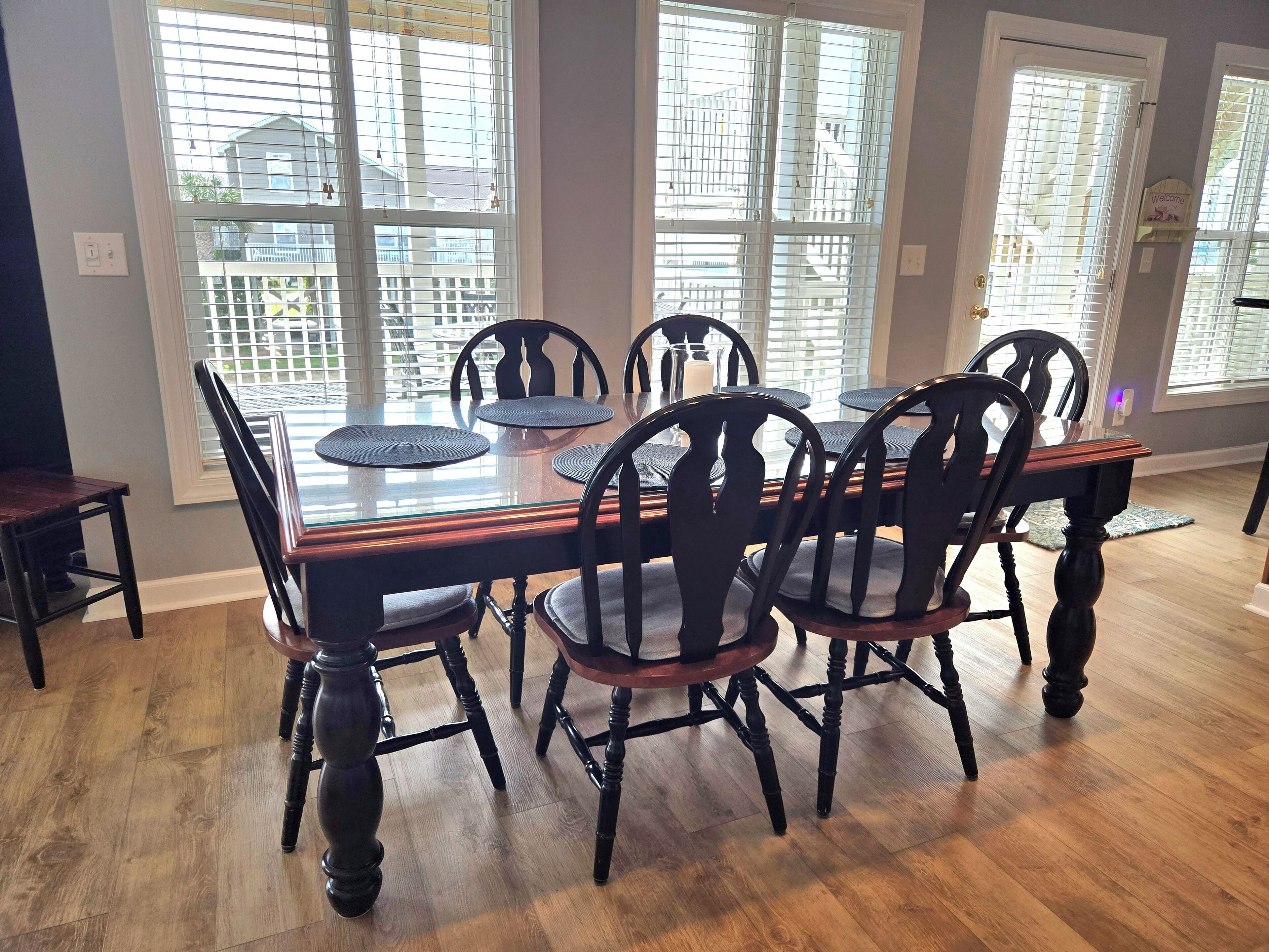 Un coin repas avec une table à plateau de verre, des chaises noires et une vue sur les bâtiments à travers de grandes fenêtres.