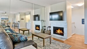 A modern living room with a fireplace, a sofa, a coffee table, and a television mounted above the fireplace. - Coastal getaway, relaxing Del Mar Townhouse steps from Torrey Pines State Beach (Del Mar)