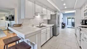A modern kitchen with white cabinetry, a stainless steel refrigerator, and a large island with a bowl. - Coastal getaway, relaxing Del Mar Townhouse steps from Torrey Pines State Beach (Del Mar)