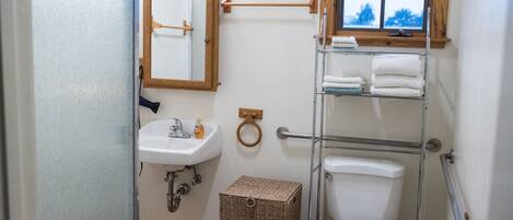 Une salle de bain avec un lavabo blanc, un miroir et des toilettes. Il y a une fenêtre au-dessus des toilettes, ainsi qu'un porte-serviettes avec des serviettes.