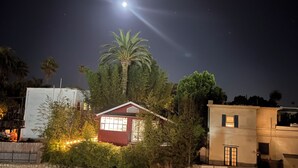 A house with a red exterior, surrounded by greenery, under a night sky with a visible moon. - Second story studio 1 1/2 blocks to beach (Santa Barbara)