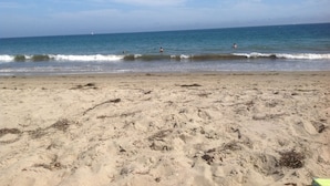 A sandy beach with waves, a clear sky, and a distant sailboat. - Second story studio 1 1/2 blocks to beach (Santa Barbara)