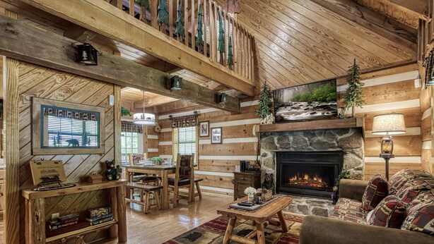 Ein gemütliches Blockhaus-Interieur mit Kamin aus Stein, Holzmöbeln und einem Fernseher an der Wand.