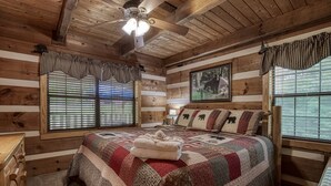 Une chambre située dans une cabane en rondins, avec un grand lit, une commode en bois et un ventilateur de plafond.