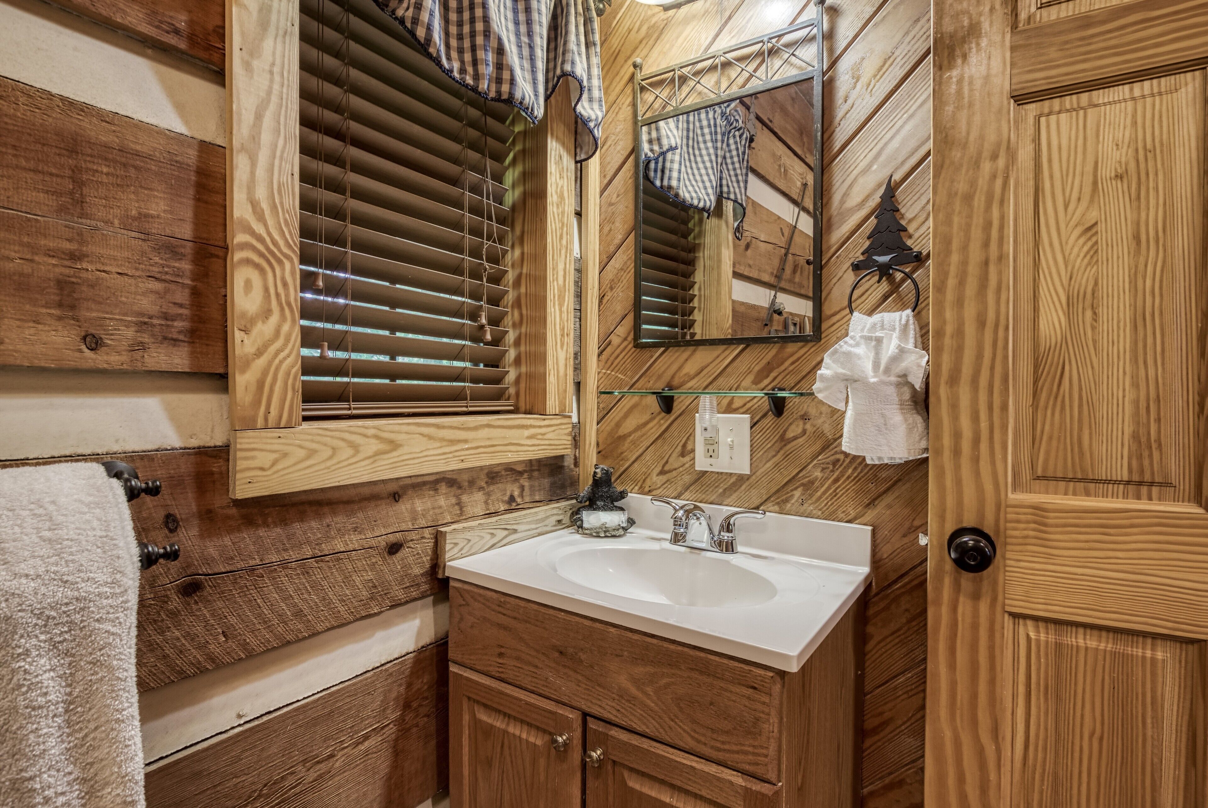 A wooden bathroom with a white sink, wooden cabinets, a mirror, and a towel rack.