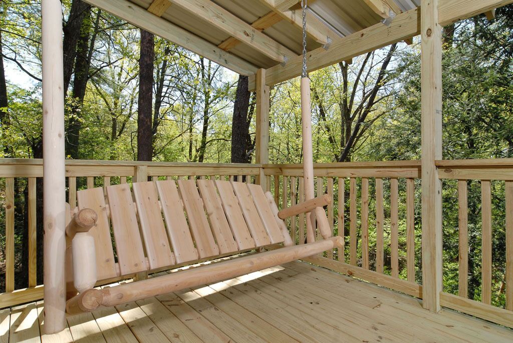 A wooden deck with a bench, surrounded by trees.