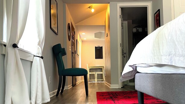 A bedroom with a bed, a chair, a red rug, and a hallway leading to a bathroom. - The Moon and the Stars Cottage- in Town! (Nashville)