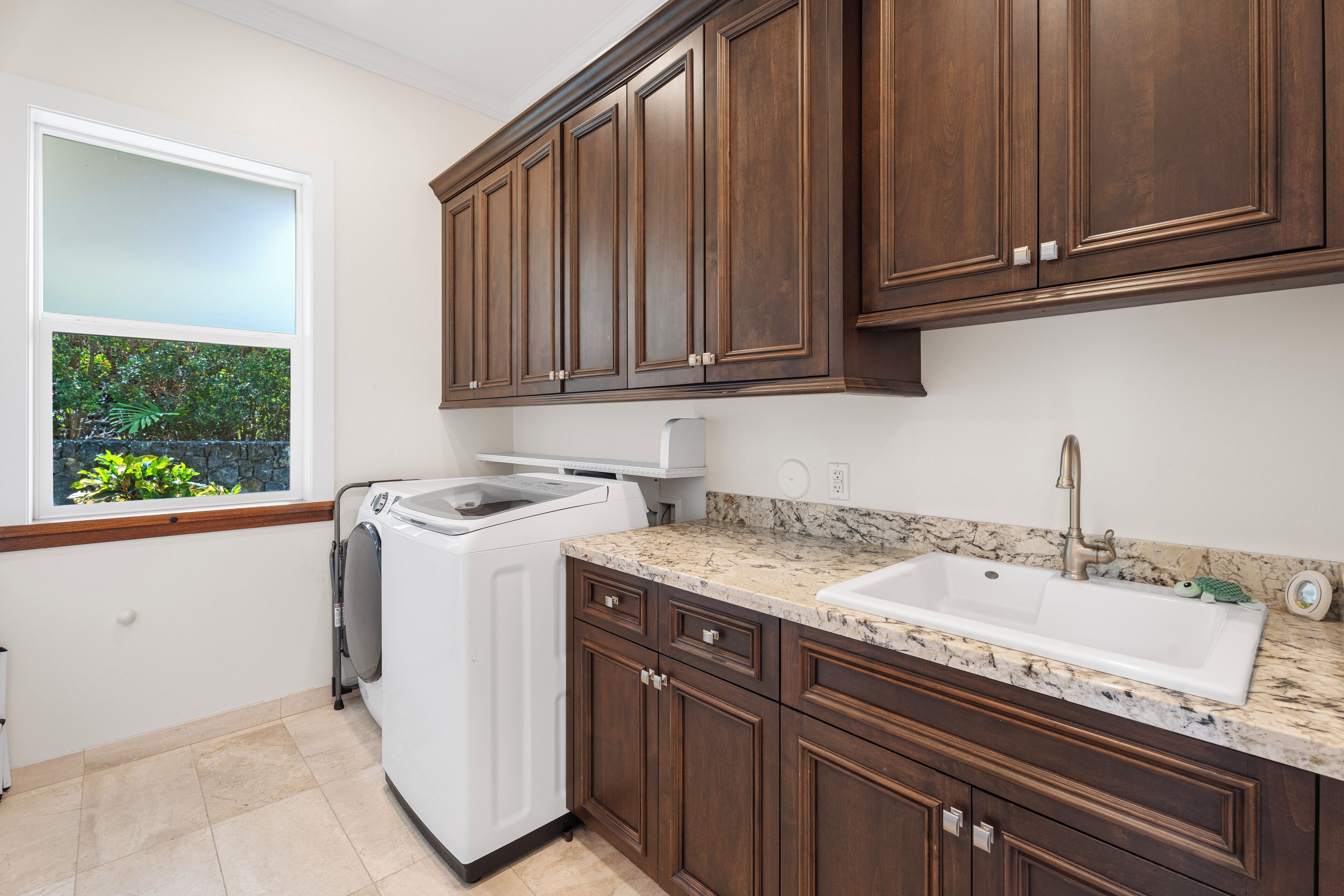 A kitchen with dark wooden cabinets, a white washing machine, a granite countertop, and a white sink.