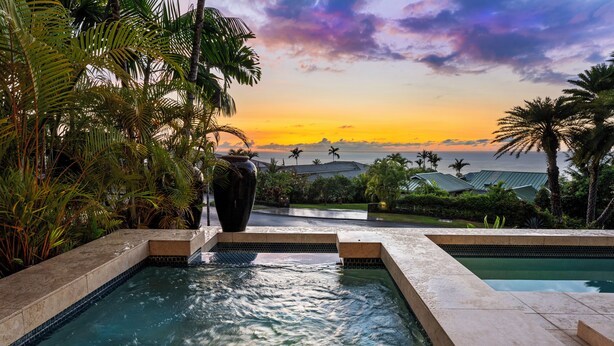Un espace piscine offrant une vue sur le coucher de soleil et les palmiers.