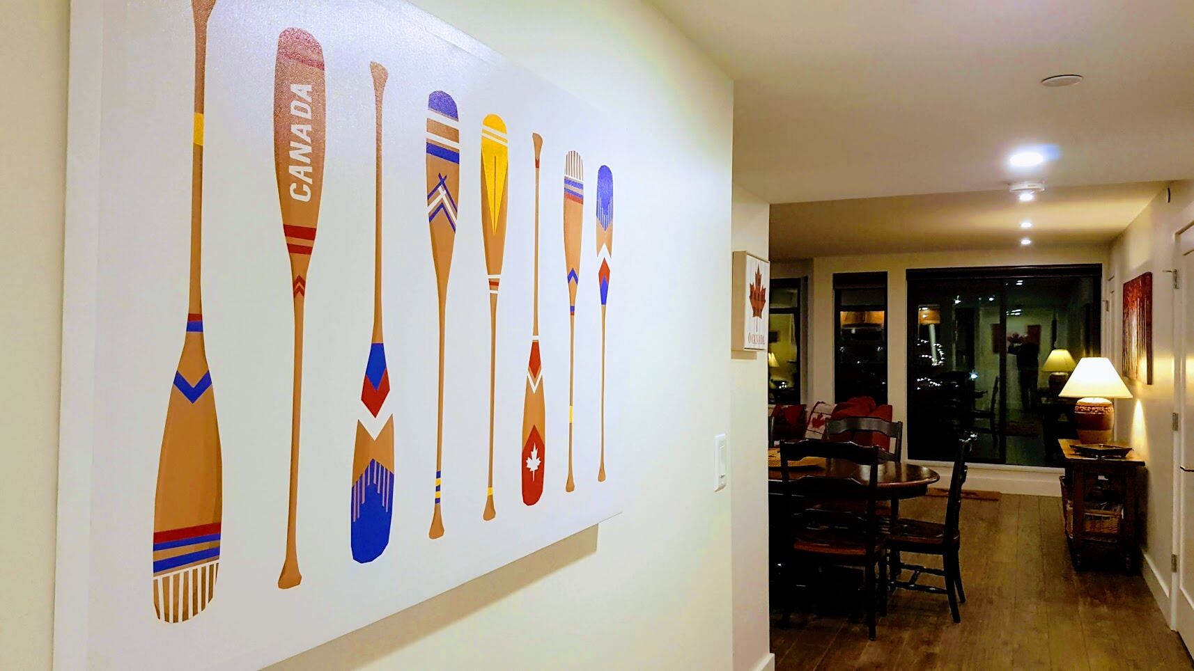 Un pasillo con una obra de arte en la pared que muestra palas, un área de comedor con sillas y una mesa, y un ventanal con vistas al exterior.