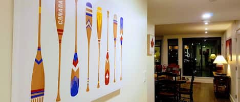 Un pasillo con una obra de arte en la pared que muestra palas, un área de comedor con sillas y una mesa, y un ventanal con vistas al exterior.