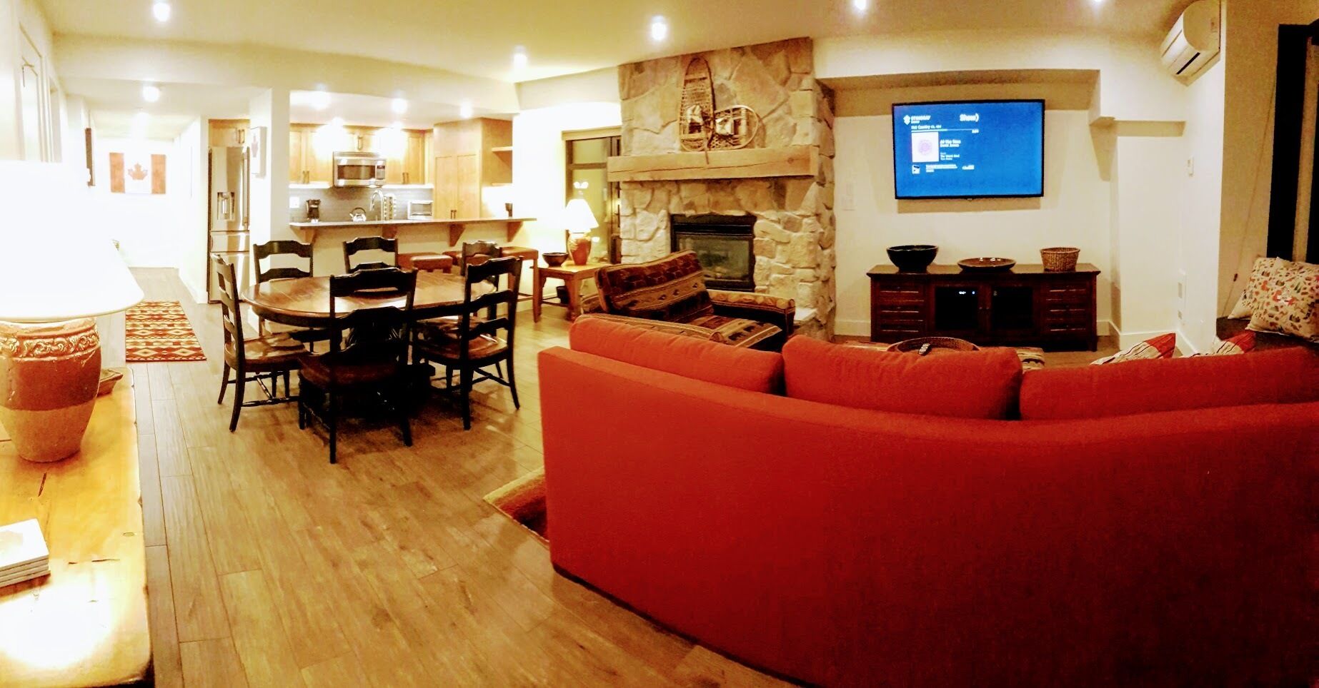 Un salon avec un canapé rouge, un coin repas avec une table et des chaises, une cheminée en pierre et un téléviseur fixé au mur.