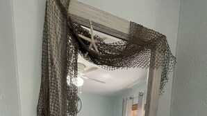 Une chambre avec un grand miroir, un lit, une plante et un petit panier en fil métallique posé sur une étagère blanche.
