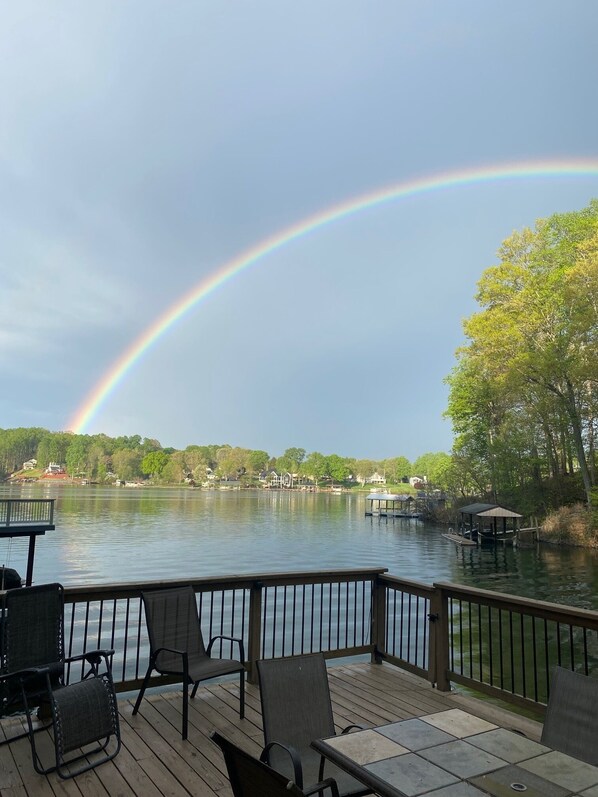 Une terrasse avec des sièges extérieurs donnant sur un lac, un arc-en-ciel et des maisons en arrière-plan.