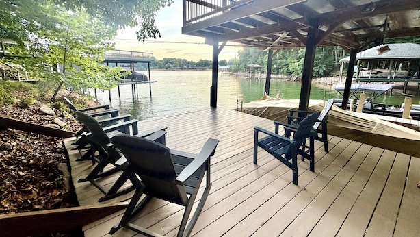 Una terraza de madera con mobiliario exterior, vistas a un lago y un área cubierta con barandilla.