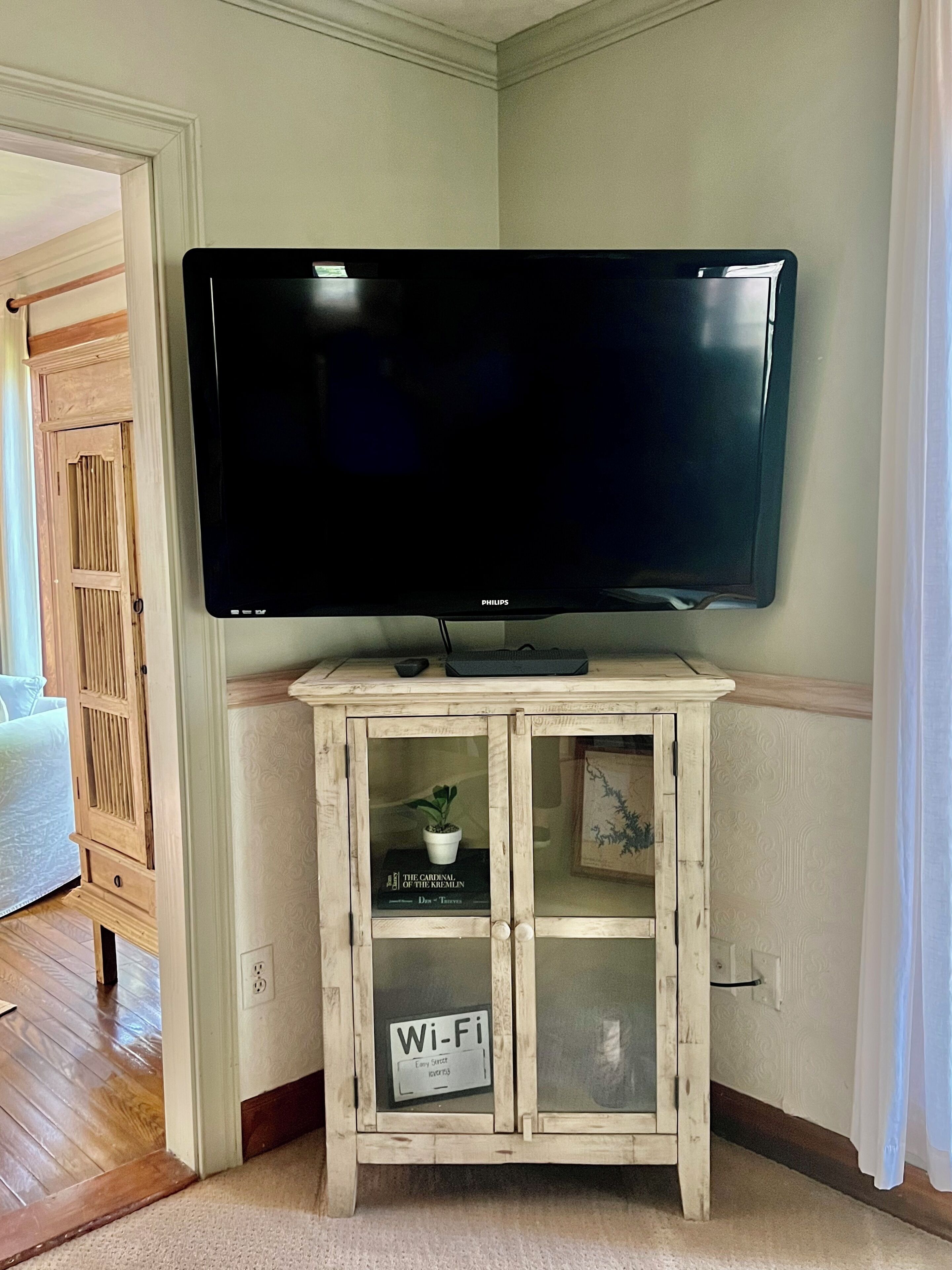 Un televisor montado sobre un mueble de madera con un símbolo de Wi-Fi, un libro y una planta pequeña en su interior.