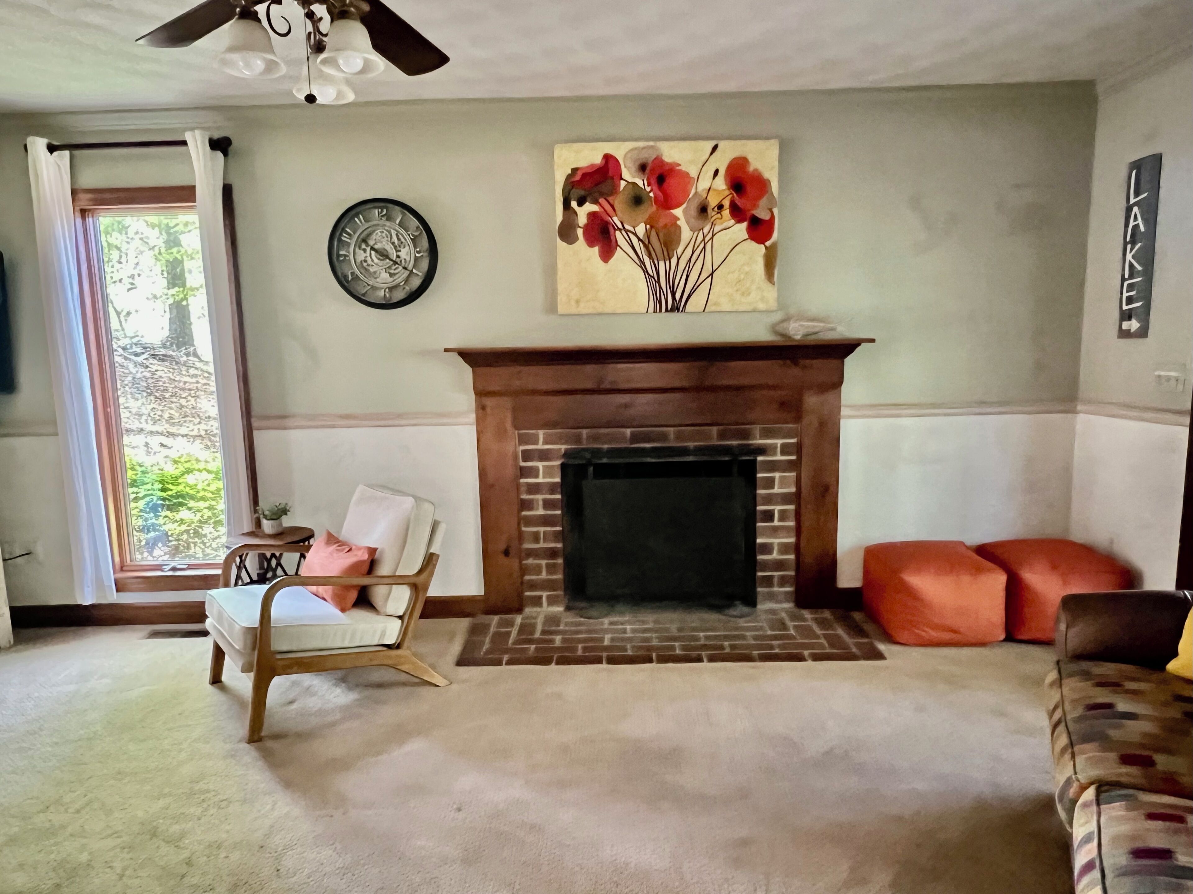 A living room with a fireplace, a clock, a painting, and a view of the outdoors.