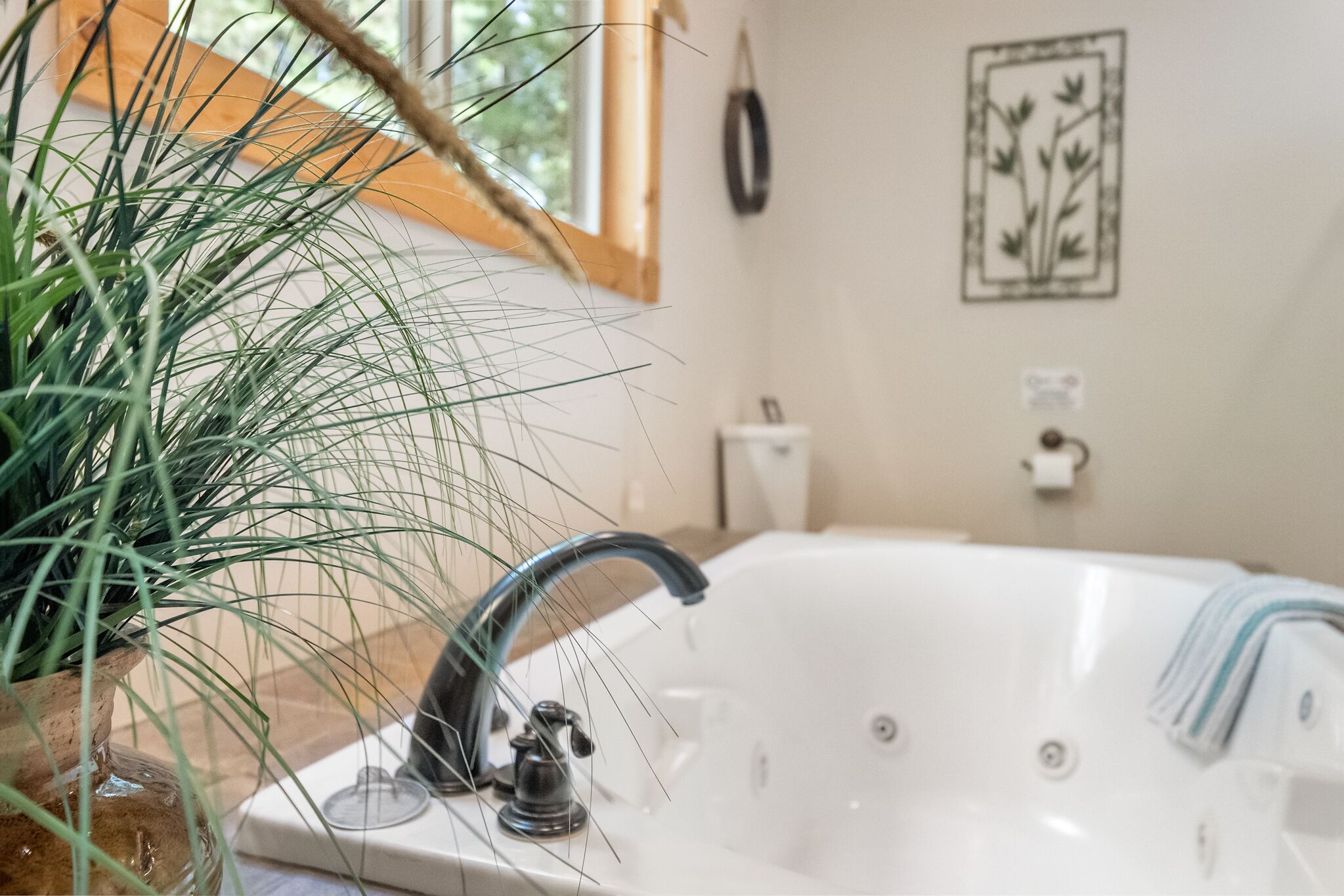 A bathroom with a white bathtub, a potted plant, and a wall-mounted toilet.