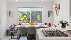 A dining area with a large window, a table set for four, and a kitchen area visible in the foreground. - The Compound: 2 Houses, 6 BR/4BA, Pool, Spa, Ping Pong, Pool Table, Events! (Indio)