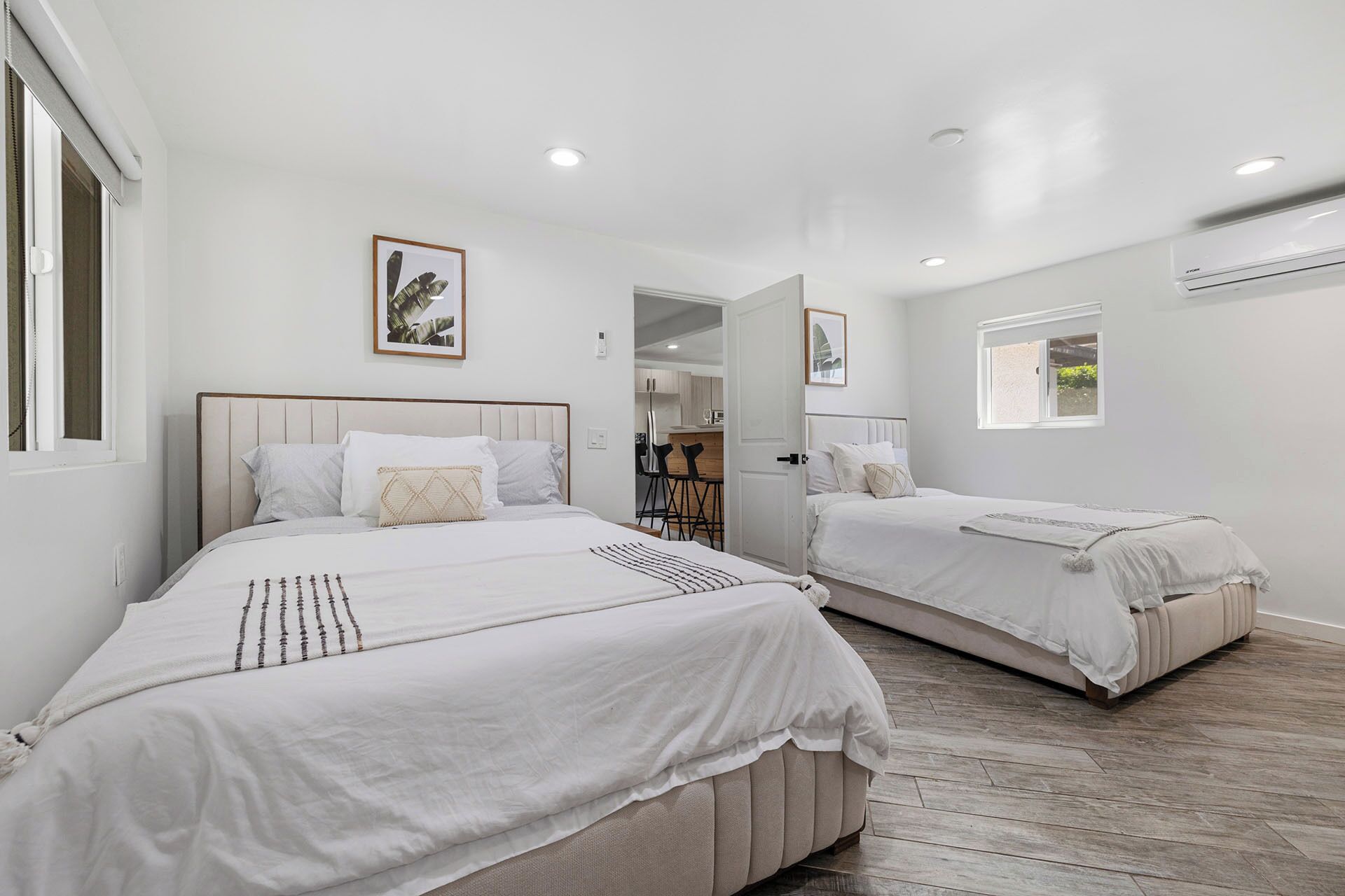 A bedroom with two beds, a wooden floor, and a small window.