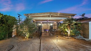 A covered outdoor patio with a brick pathway leading to a seating area under a pergola. - The Compound: 2 Houses, 6 BR/4BA, Pool, Spa, Ping Pong, Pool Table, Events! (Indio)