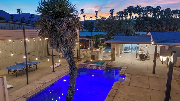 An outdoor pool area with a stone structure, string lights, and a dining setup. - The Compound: 2 Houses, 6 BR/4BA, Pool, Spa, Ping Pong, Pool Table, Events! (Indio)