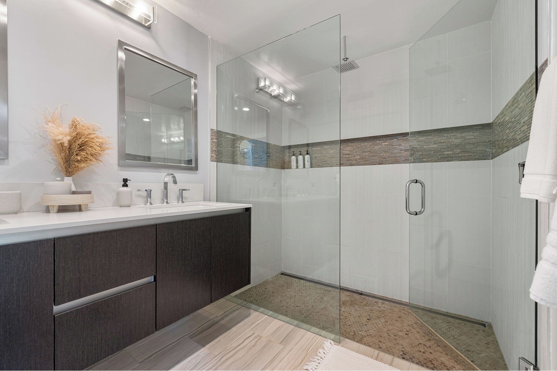 A modern bathroom with a glass shower enclosure, a large mirror, and a vanity with dark cabinetry.