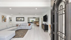 A modern living room with a sectional sofa, a dining area, and a kitchen in the background. - The Compound: 2 Houses, 6 BR/4BA, Pool, Spa, Ping Pong, Pool Table, Events! (Indio)