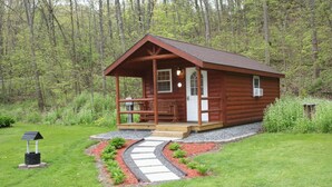 A wooden cabin with a porch, surrounded by a garden and a forest.