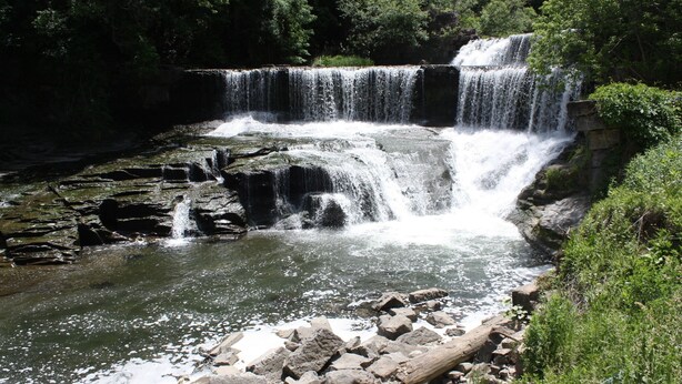 A waterfall cascading over rocks into a pool, surrounded by greenery.