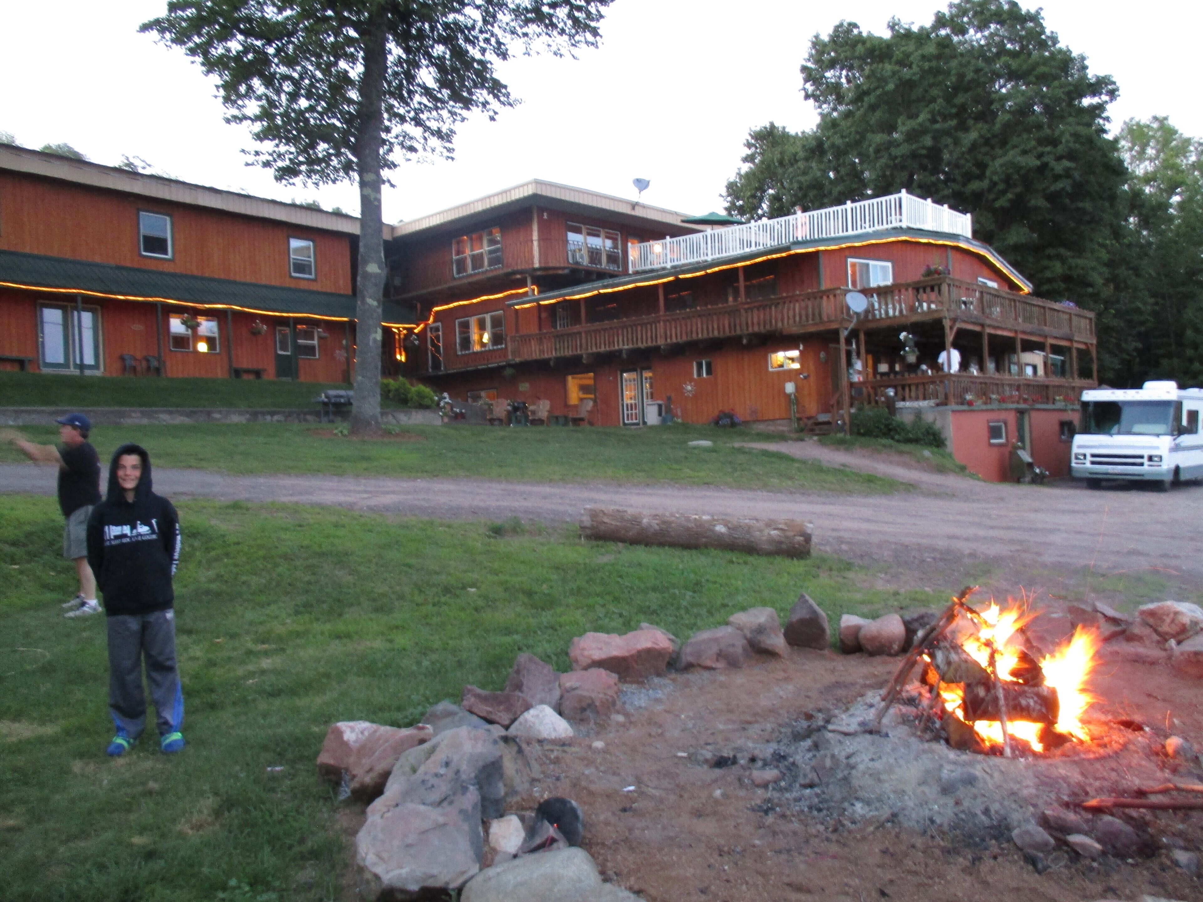 A lodge with a wooden exterior, a deck, and a fire pit in the foreground.
