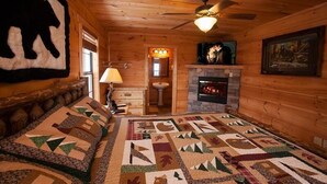 L’intérieur d’une cabane en rondins, avec un lit recouvert d’une courtepointe, une cheminée et une décoration murale représentant la silhouette d’un ours.