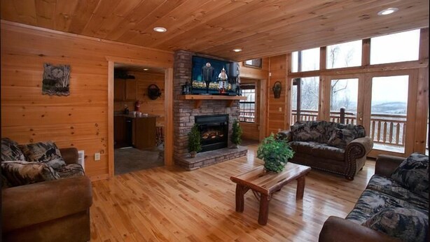 L’intérieur d’une cabane en rondins, avec une cheminée, un plancher en bois et une vue dégagée grâce à de grandes fenêtres.
