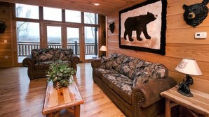 L’intérieur d’une cabane avec des murs en bois, une grande fresque représentant un ours, deux canapés à motifs, une table basse en bois et une vue dégagée sur le paysage grâce à de grandes fenêtres.