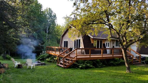 Une maison avec une terrasse en bois, un espace salon extérieur et un arbre dans le jardin.