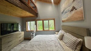 Une chambre avec un grand lit, une télévision, une fenêtre donnant sur des arbres et un tableau accroché au mur.