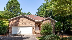 A two-story brick house with a white garage door, surrounded by trees and greenery. - Golf front home with 8 beds (Pinehurst)