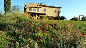 A stone house with a sloped roof, surrounded by a lush garden with various flowering plants. - FARMH. PODERE CUNINA 25 KM SUD SIENA DI FRONTE AL MONTALCINO PRENDENDO LEZIONI DI CUCINA (Buonconvento)