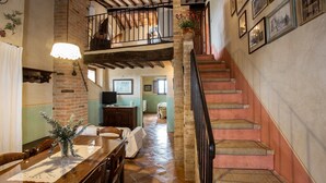 A spacious dining area with a wooden table and chairs, a brick wall, and a staircase leading to an upper level. - FARMH. PODERE CUNINA 25 KM SUD SIENA DI FRONTE AL MONTALCINO PRENDENDO LEZIONI DI CUCINA (Buonconvento)