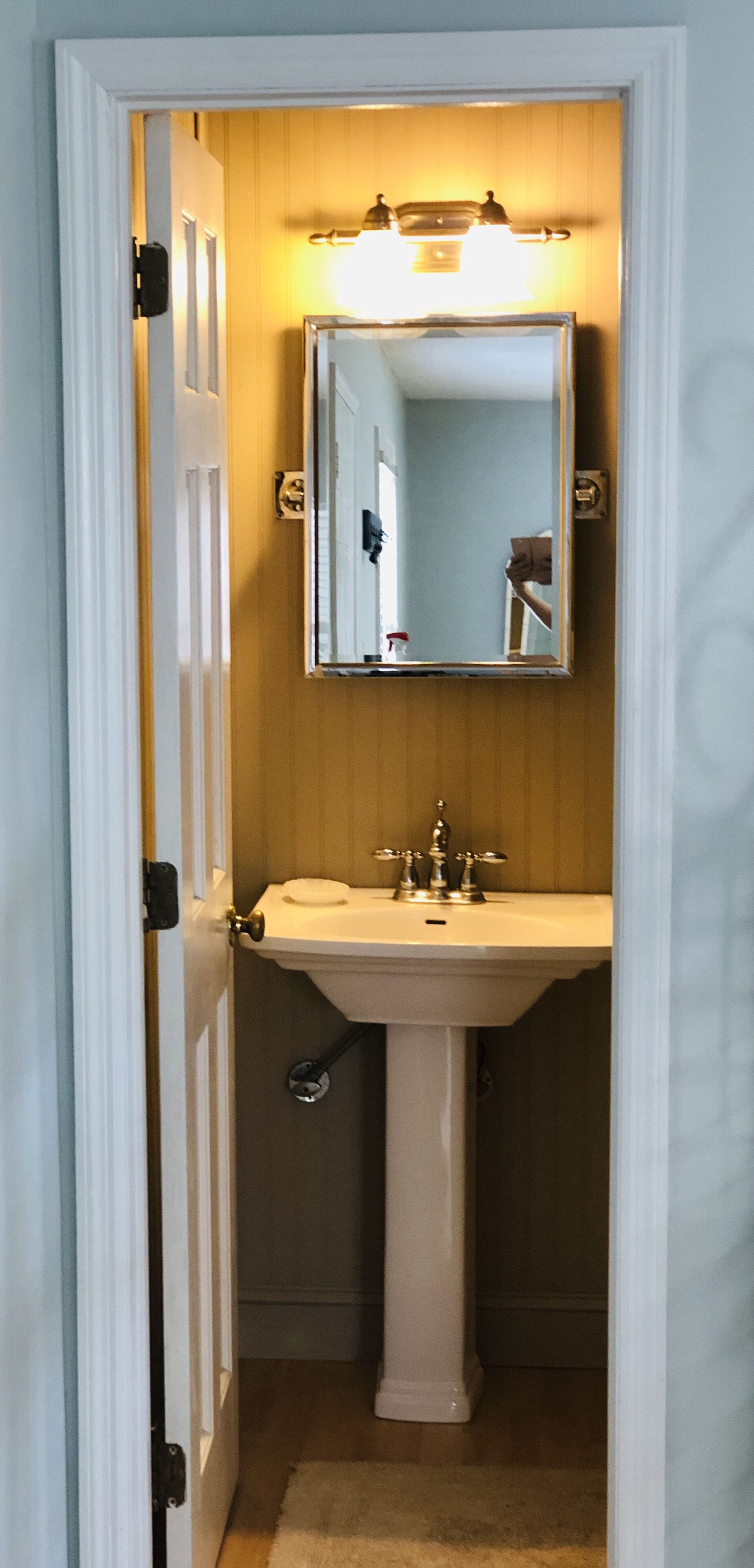 Une salle de bain avec un lavabo blanc, un miroir et un luminaire placé au-dessus du miroir.
