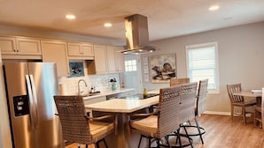 A modern kitchen with a stainless steel refrigerator, a central island with bar stools, and a dining area with wooden chairs. - Oceanfront Duplex - Sleeps 10 - Great Price!! 3 B/R, 2.5 bath, outdoor shower (Atlantic Beach)
